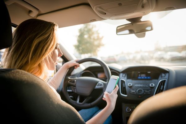 Young woman looking to her smartphone while driving car 