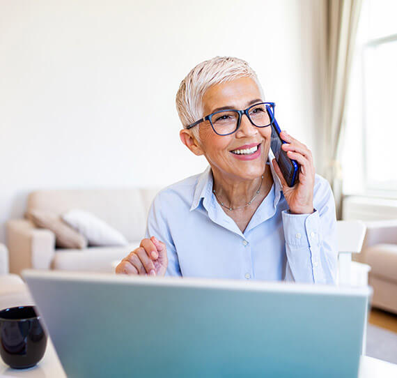 woman talking on phone seated in front of laptop