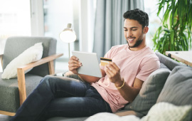 Person on a couch holding a tablet and a credit card